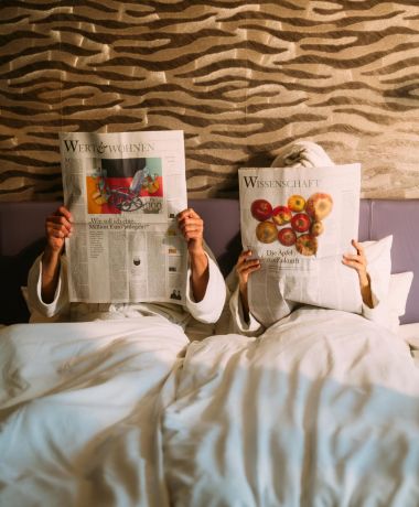 Design Zimmer im Boutique Hotel am Wolfgangsee Paar liest Zeitung im Bett eines Design Zimmers im Boutique Hotel am Wolfgangsee